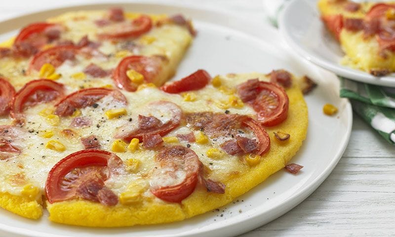 Pizza con base de polenta con salami, maíz y tomate