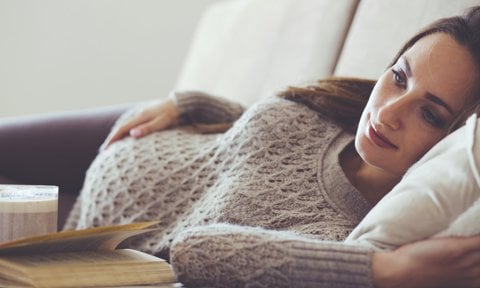 Embarazada acariciando tripa tumbada en un sofá