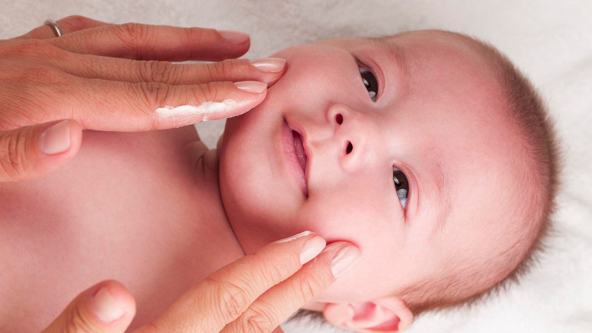 Madre echa crema en la cara a su bebé