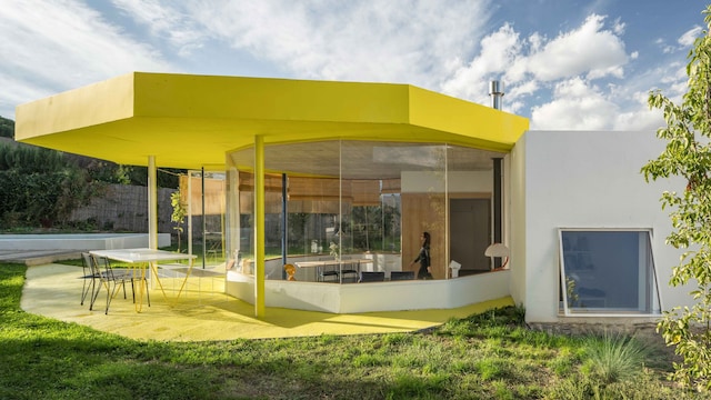 Casa con piscina, grandes ventanales, estructura amarilla, jardín y zona de comedor exterior