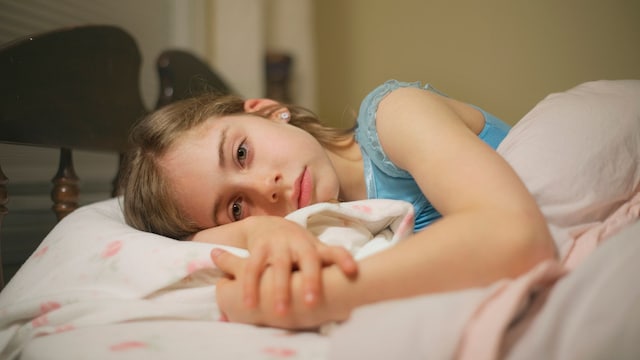 Niña con los ojos abiertos tumbada en su cama