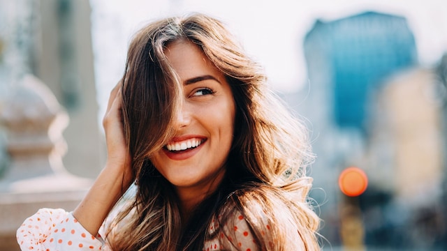 Mujer sonriendo con el flequillo tapándole media cara, blusa de manga larga de lunares en la calle