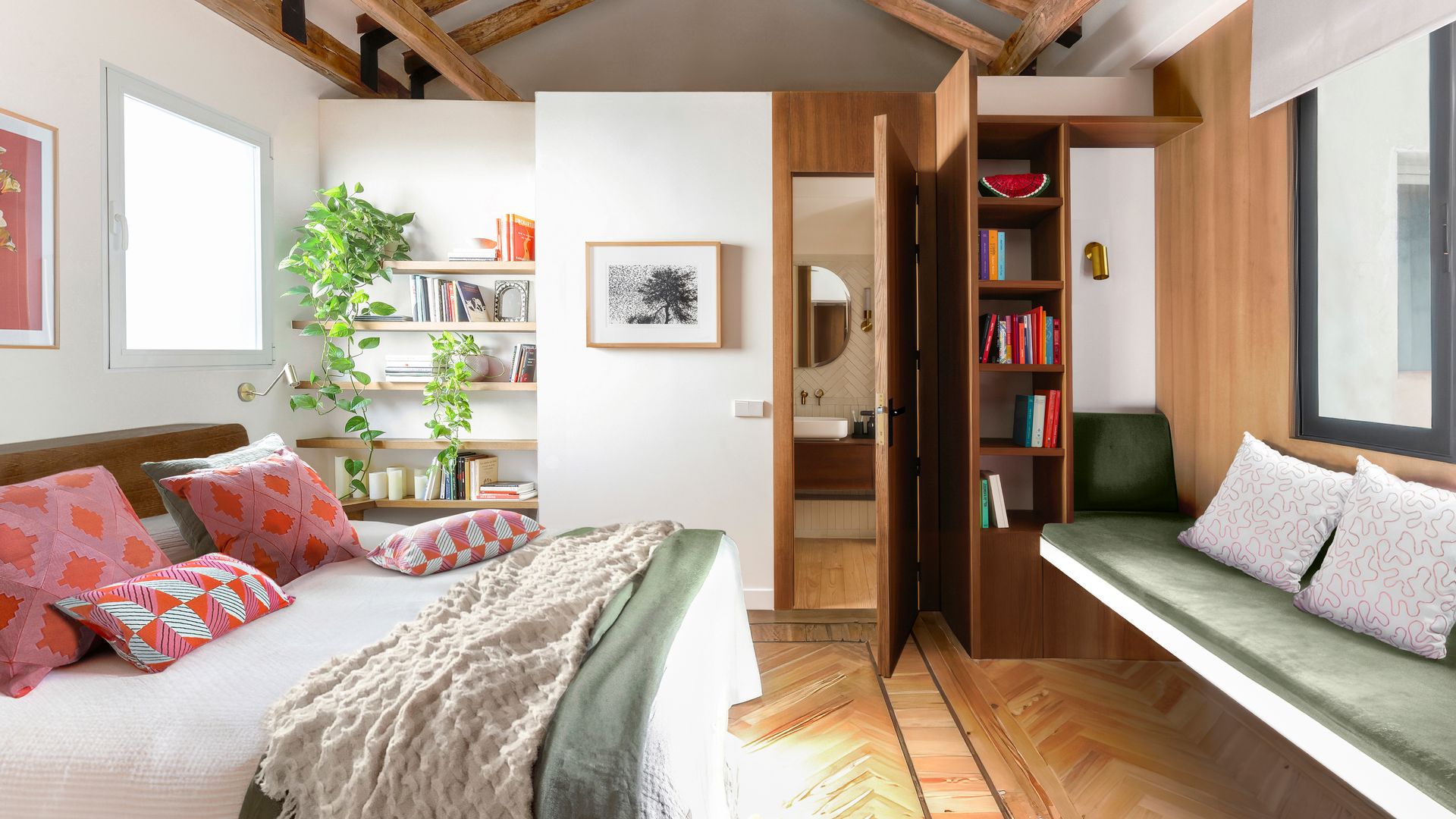 Dormitorio en suite, amplio, con techo de madera abuhardillado, baldas de madera en la pared con plantas y libros, banco bajo la ventana, estantería de madera oscura 
