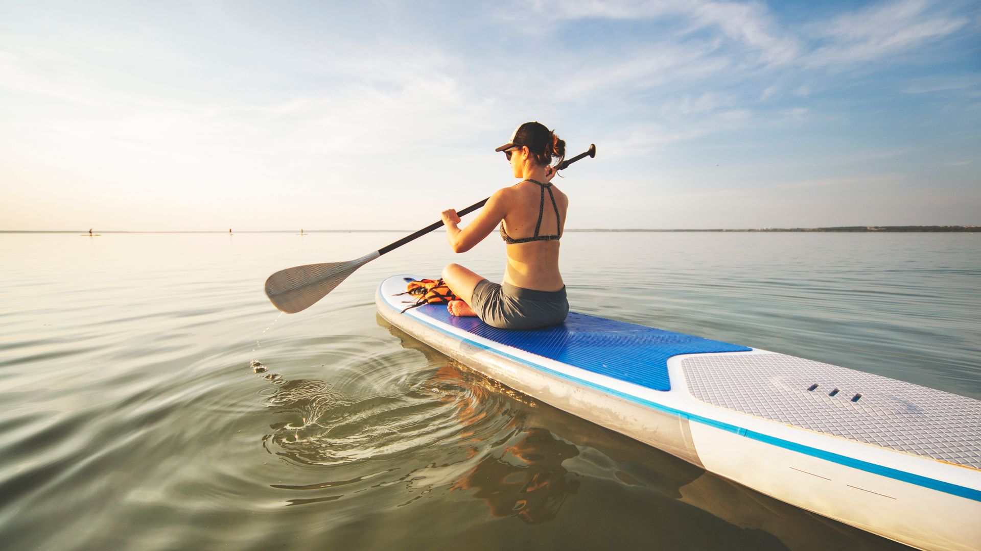 Mujer joven sentada en una tabla de paddle surf sobre el mar