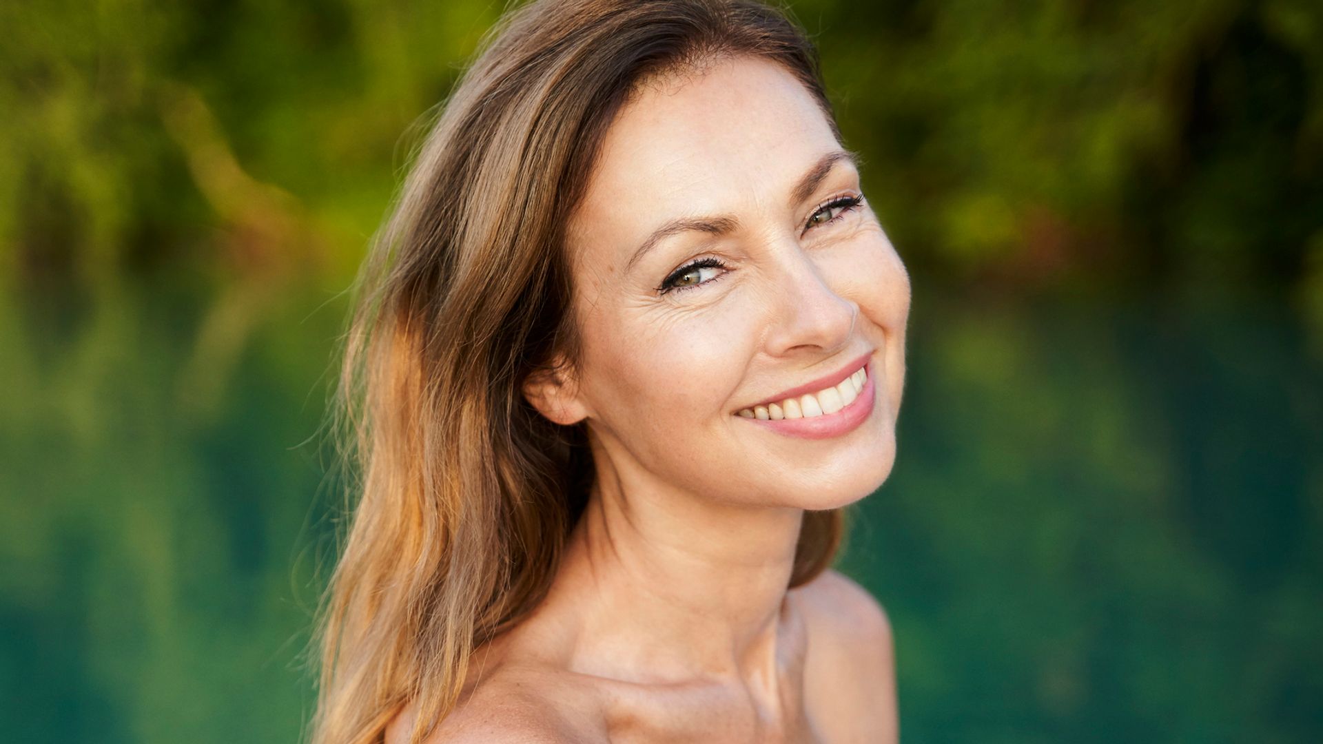 Rostro de mujer madura sonriente con pelo largo castaño frente a un lago