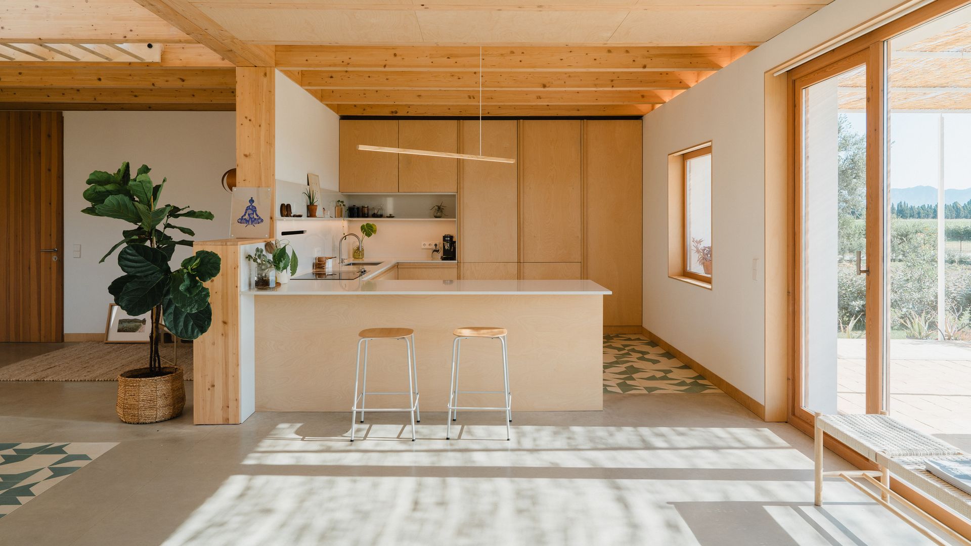 Cocina abierta con grandes ventanales, vigas de madera, cocina blanca y de madera, península con taburetes