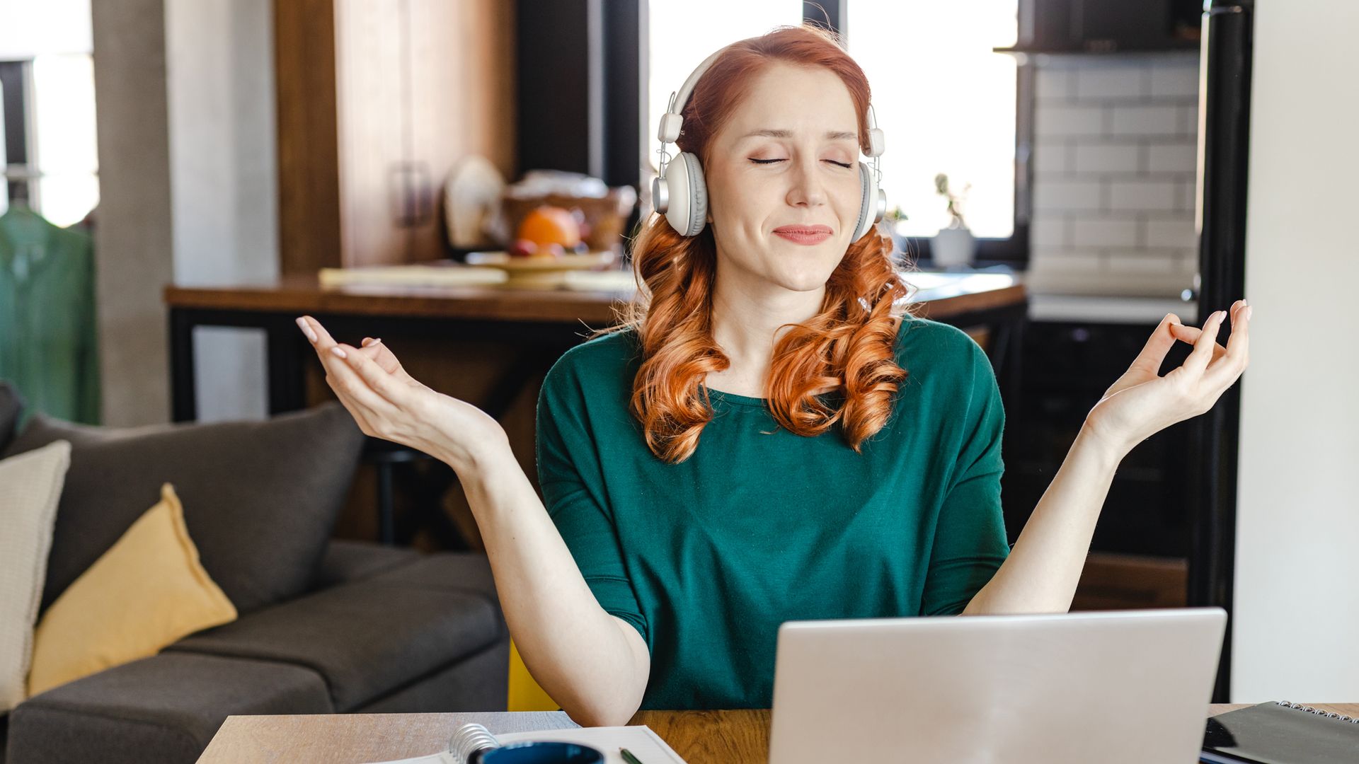 mujer meditando relajada con unos cascos frente a su ordenador