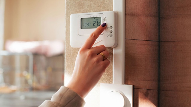 Una mujer pulsando un termostato en una casa