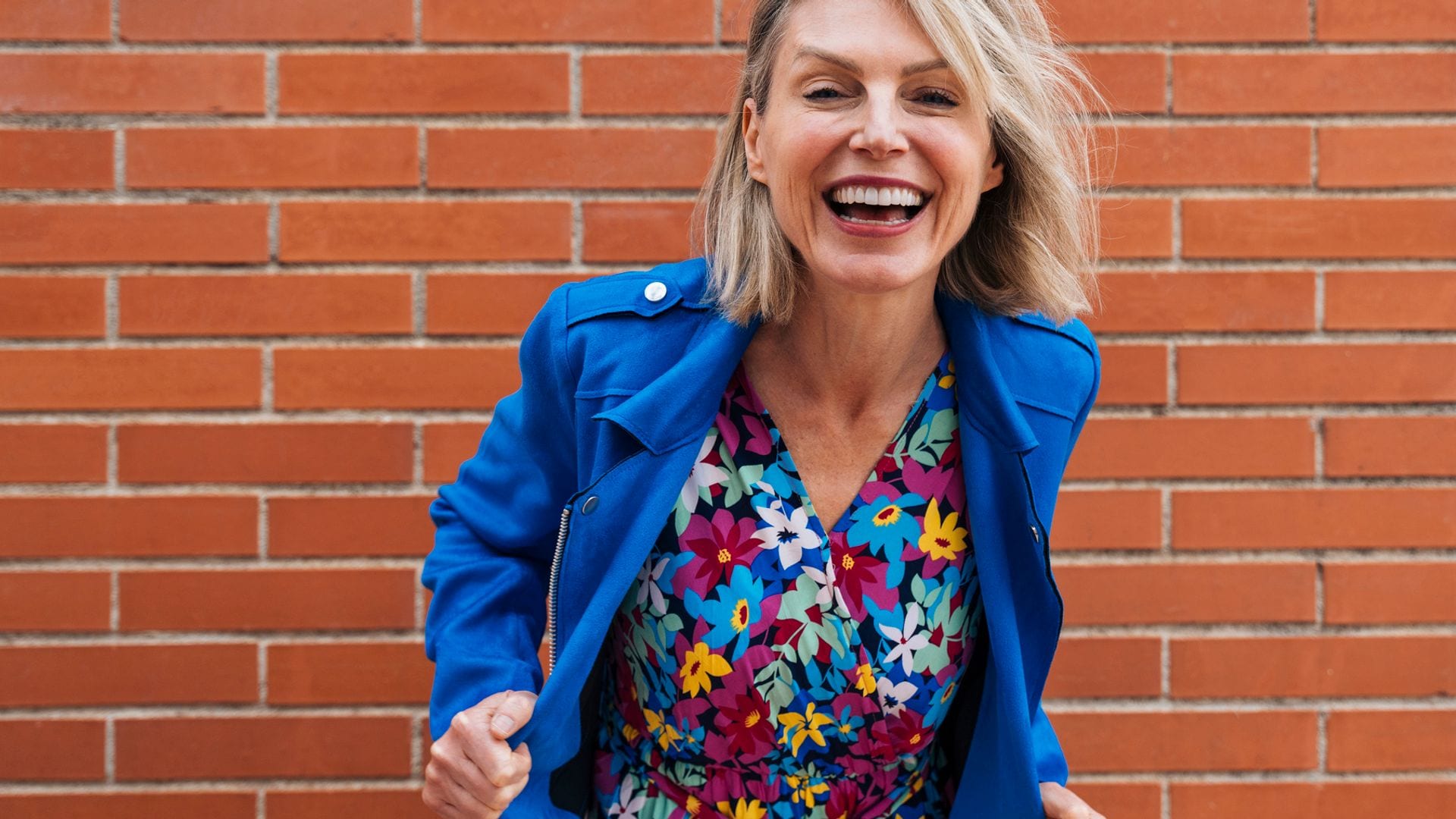 Mujer de 50 años sonriente mirando a la cámara con un vestido floral y una gabardina en azul klein.