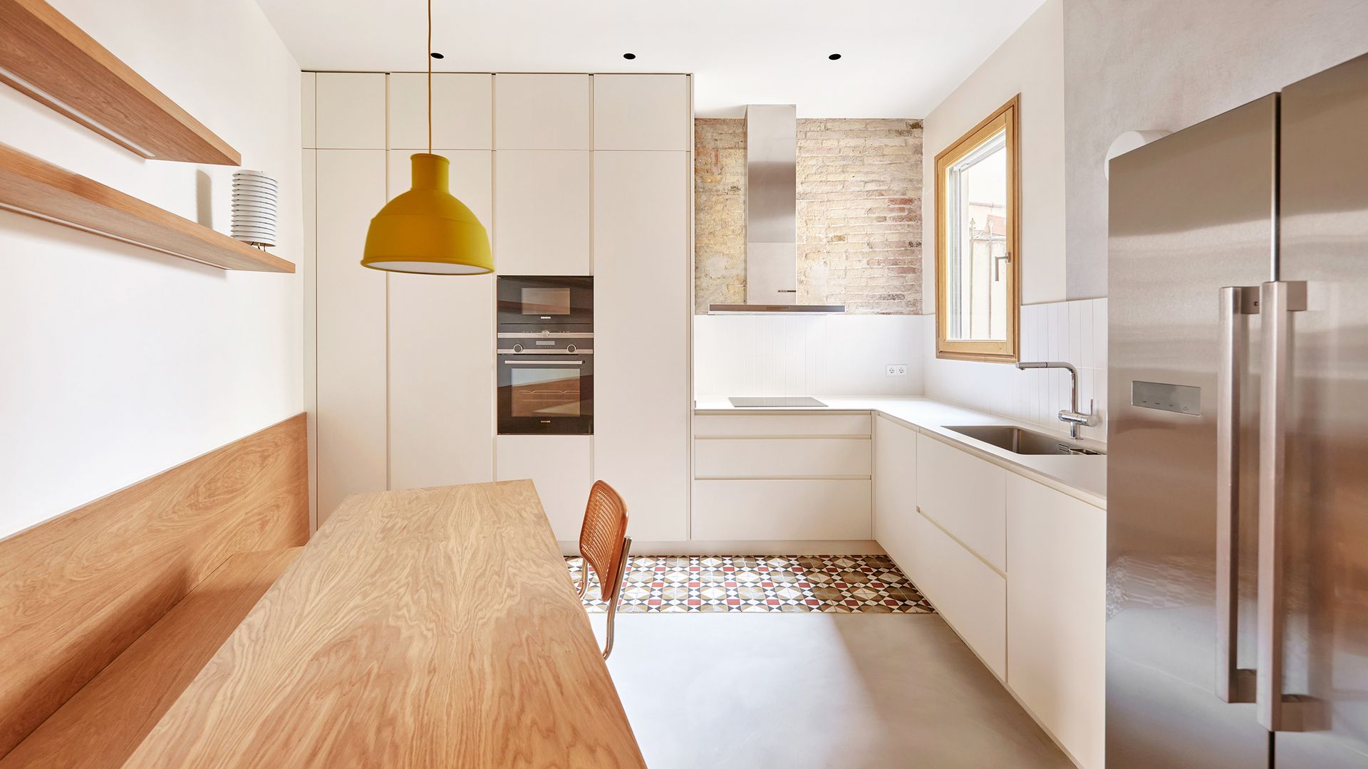 Cocina blanca con comedor, banco de madera, bóveda catalana, suelo hidráulico, lámpara de techo amarillo, frigorífico de acero, pared de ladrillo