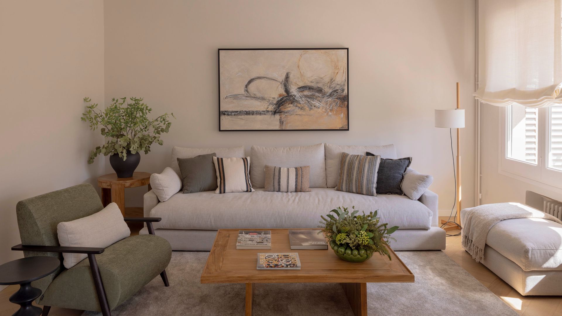 Salón con estor blanco, alfombra sofá blanco con cojines, cuadro en la pared del sofá, butacas y puf 