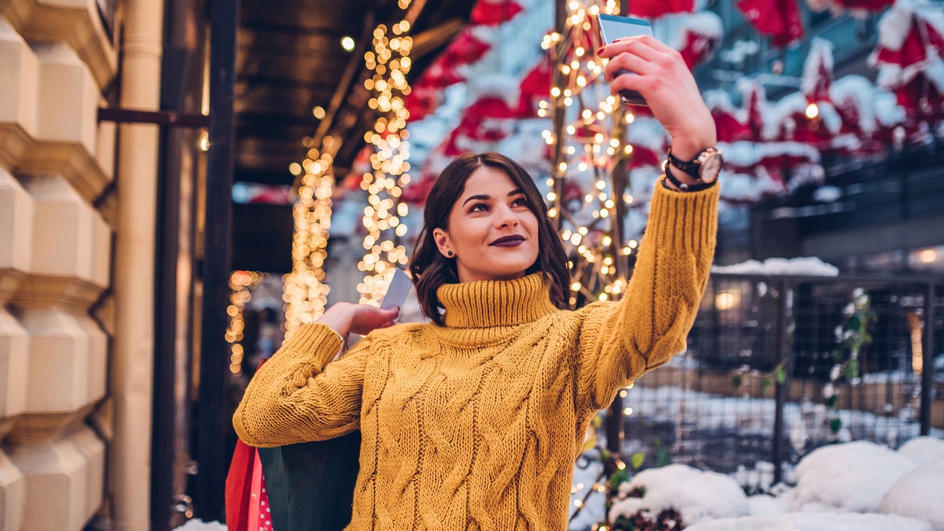 Chica haciendo un 'selfie' en la calle con ropa de invierno y decoración navideña.