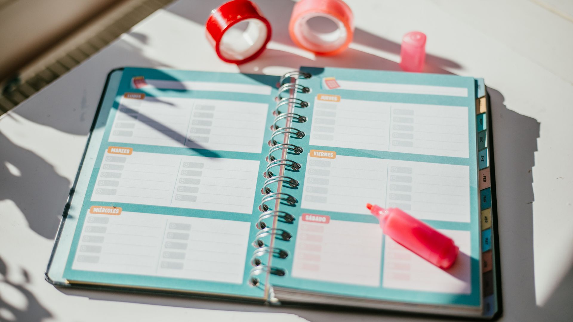 Imagen de una agenda escolar sobre un escritorio con rotuladores y subrayadores, además de 'washi tape', al atardecer. 