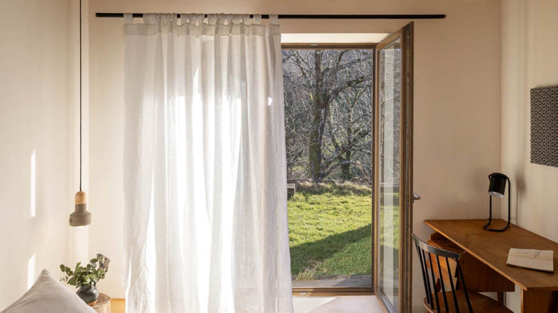 Dormitorio con cortinas blancas transparentes, escritorio y silla de madera, ropa de cama blanca, lámpara de techo