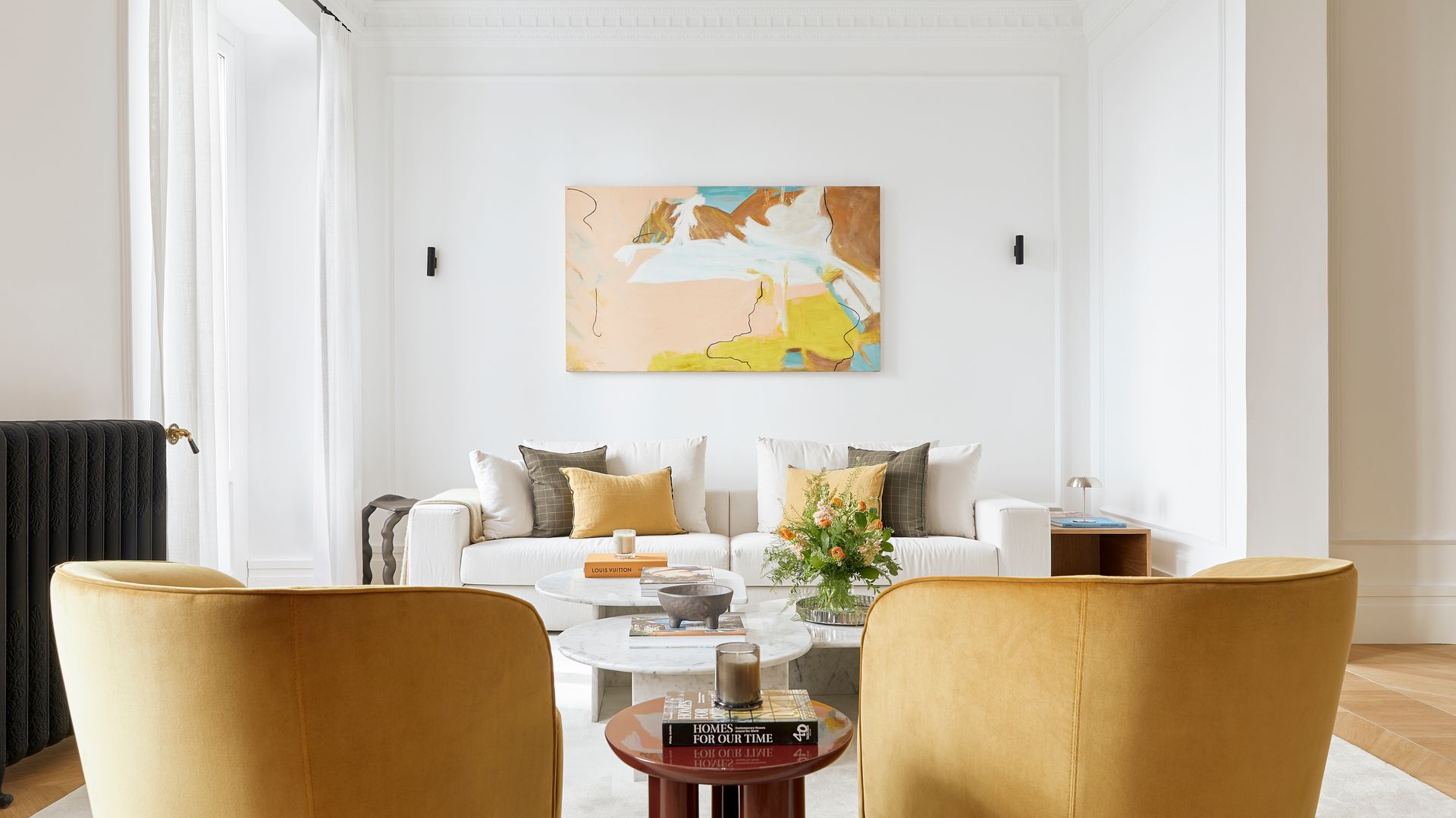 Salón con sofá blanco, cuadro en la pared del cabecero, alfombra, sillones amarillos, cortinas, radiador negro