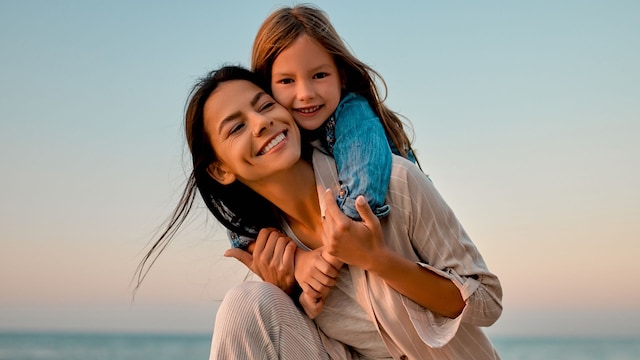 Madre con su hija en brazos felices en la playa