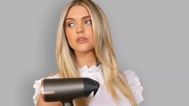 Mujer rubia con blusa blanca y vaqueros sosteniendo un secador de pelo Remington