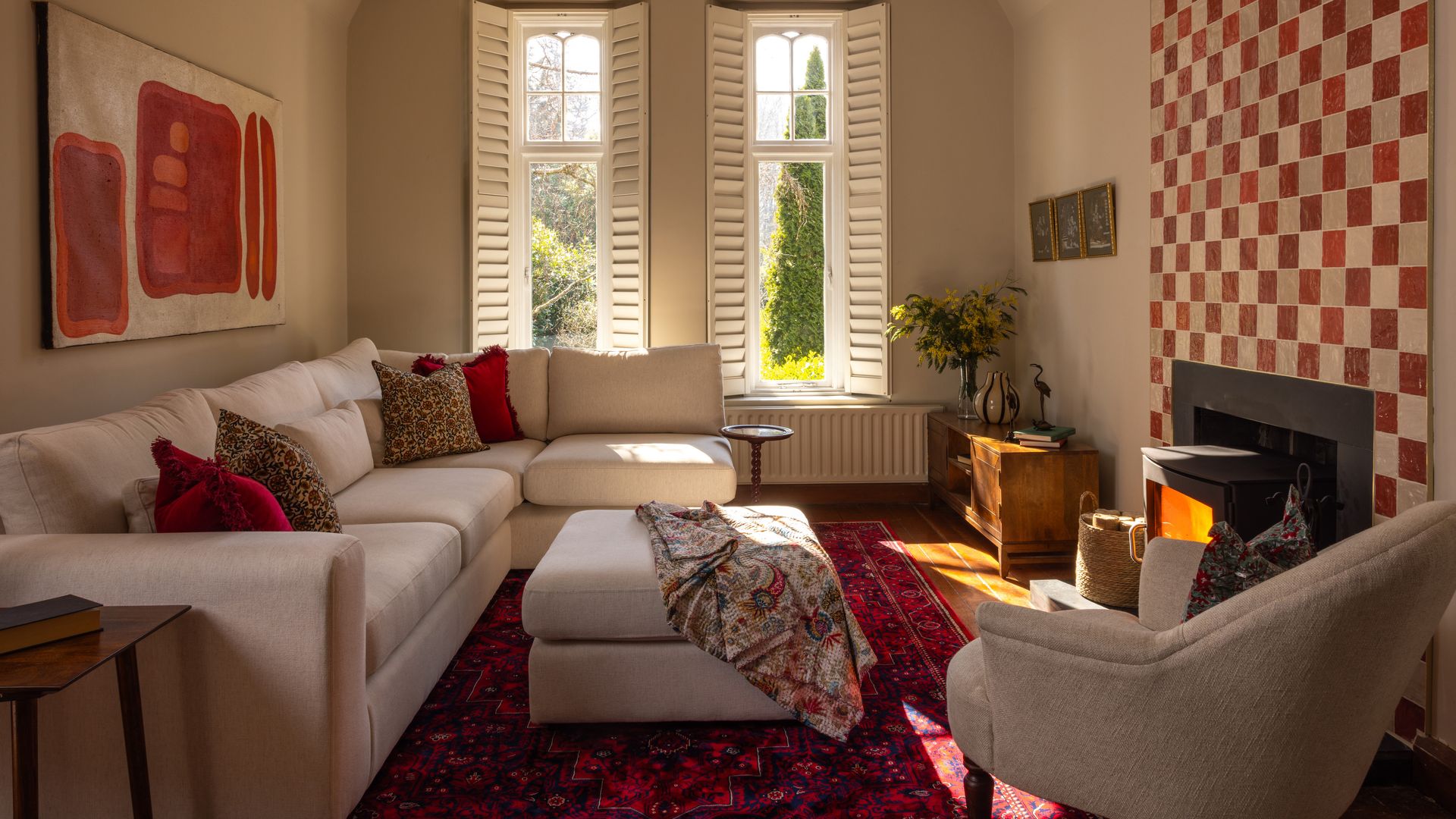 Salón con chimenea con sofá blanco, pared de la chimenea de azulejos blancos y rojos, alfombra roja, mesa de centro tapizada, cojines rojos, cuadro sobre el sofá