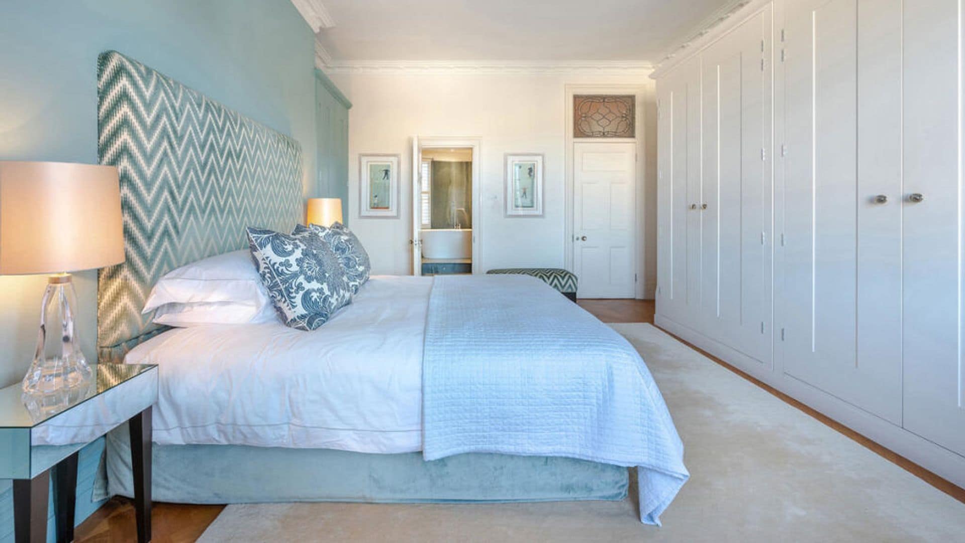 Dormitorio con pared azul claro, cabecero tapizado con diseño geométrico, pared de armarios en blanco, alfombra