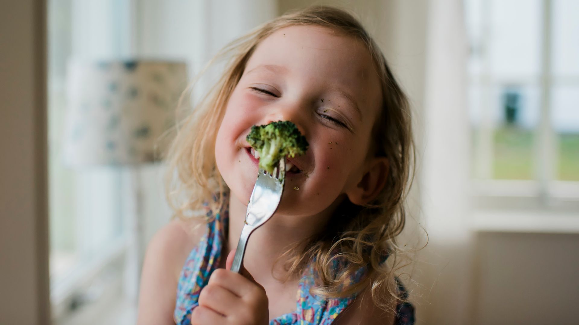 Niña pequeña tomando brócoli sonriente