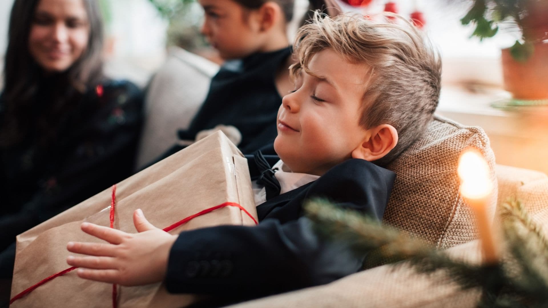 Niño sonriendo tumbado en el sofá del salón con un regalo de Navidad entre las manos.