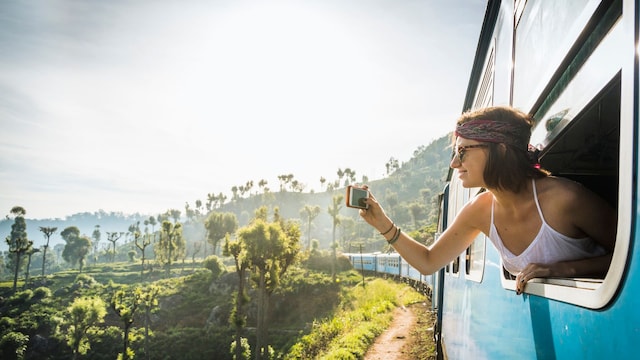 Chica joven viajando en tren mientras hace fotografías asomada a la ventana de uno de los vagones