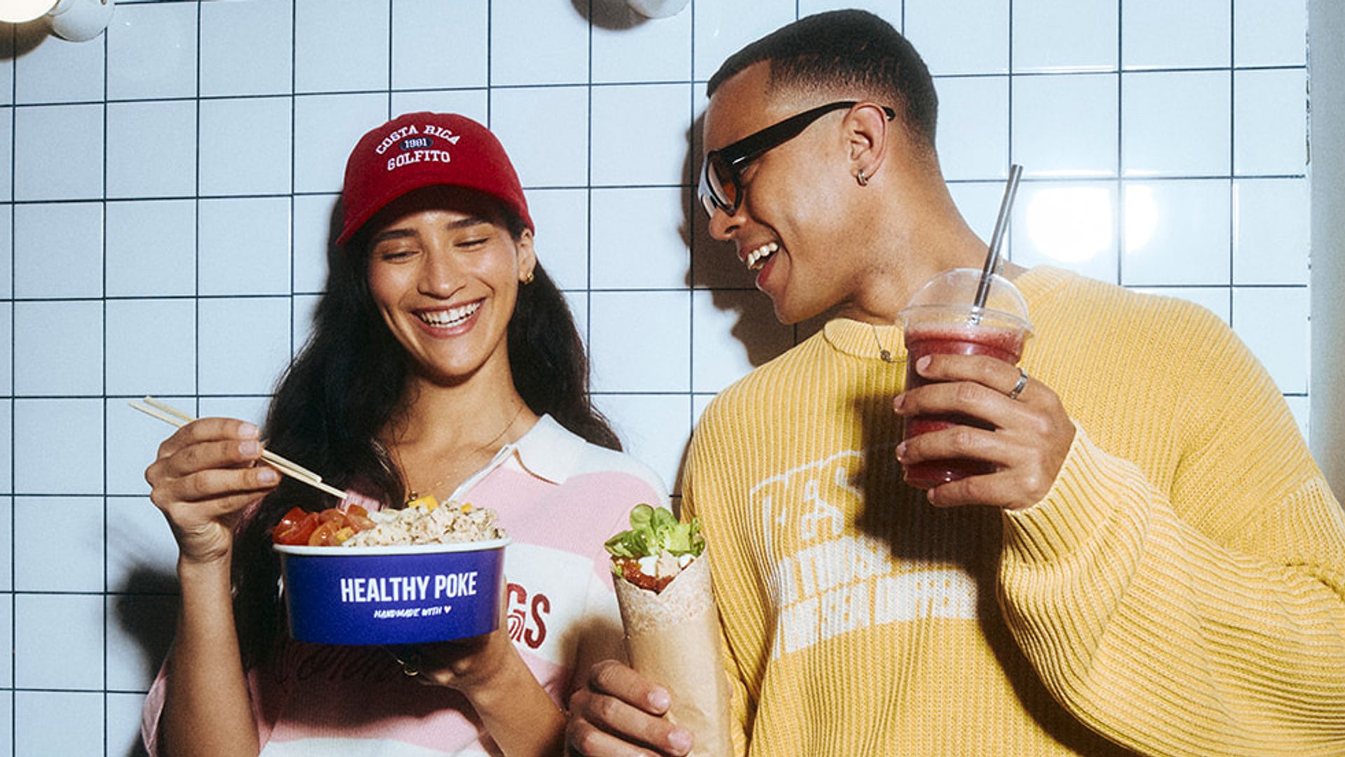 Imagen de campaña de HEALTHY POKE 2026: dos amigos sonrientes comiendo poke bowl y burrito