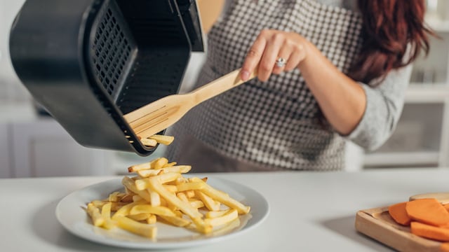 Una mujer llenando un plato de patatas fritas desde una freidora de aire