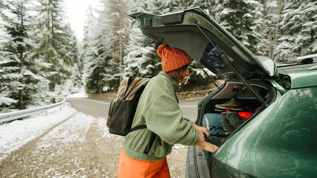 Mujer en la montaña en pleno invierno metiendo las maletas en el maletero del coche con una mochila en la espalda