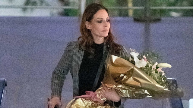 Plano medio de Eva González saliendo de la estación de tren con su equipaje y un ramo de flores