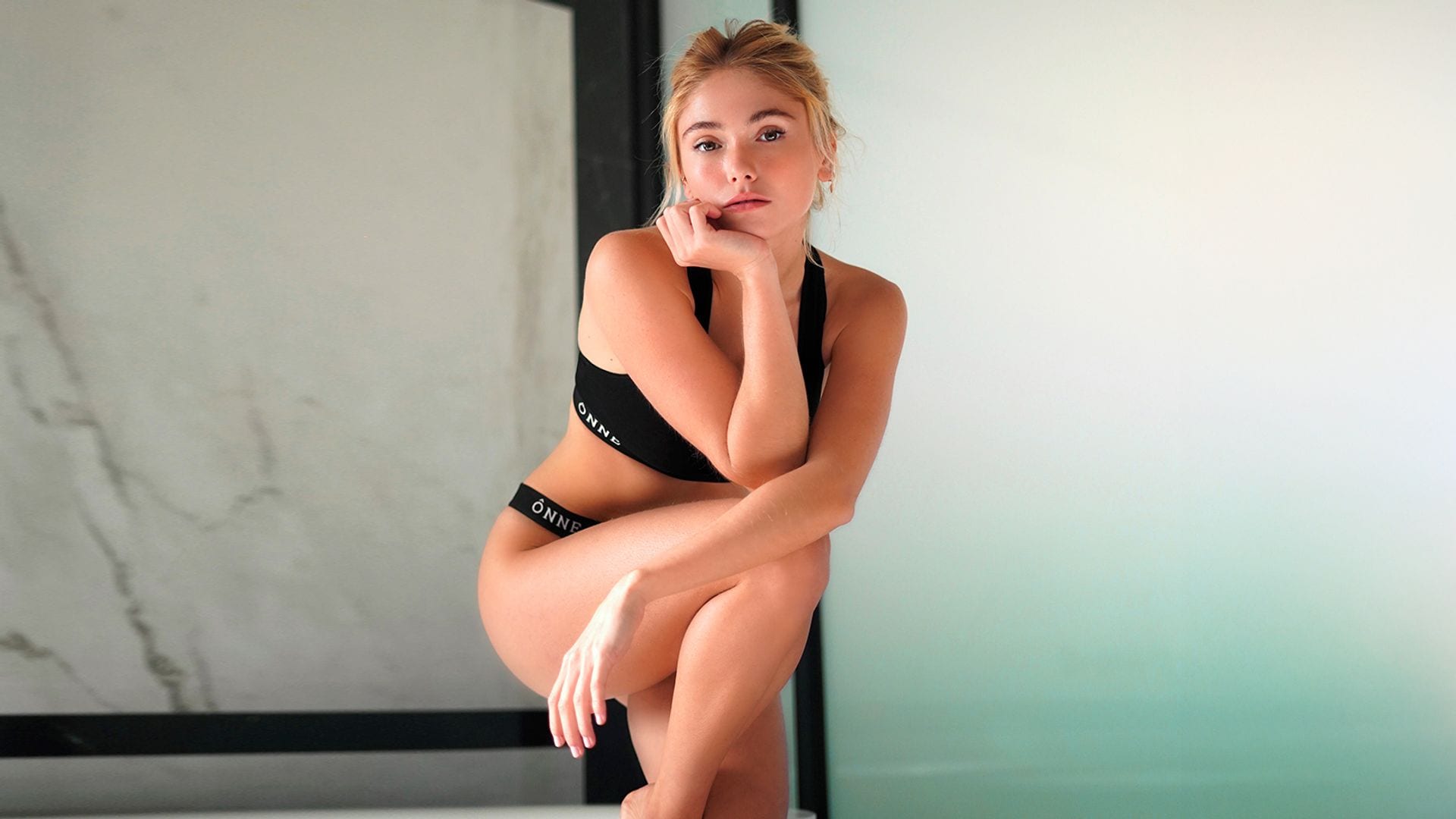 Mujer rubia en ropa interior apoyada sobre una pared con la pierna doblara