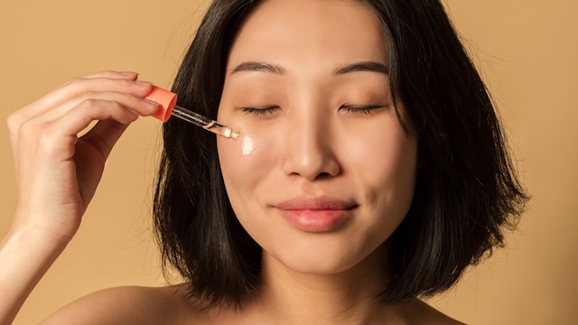 Rostro de mujer asiática aplicándose un sérum facial con los ojos cerrados