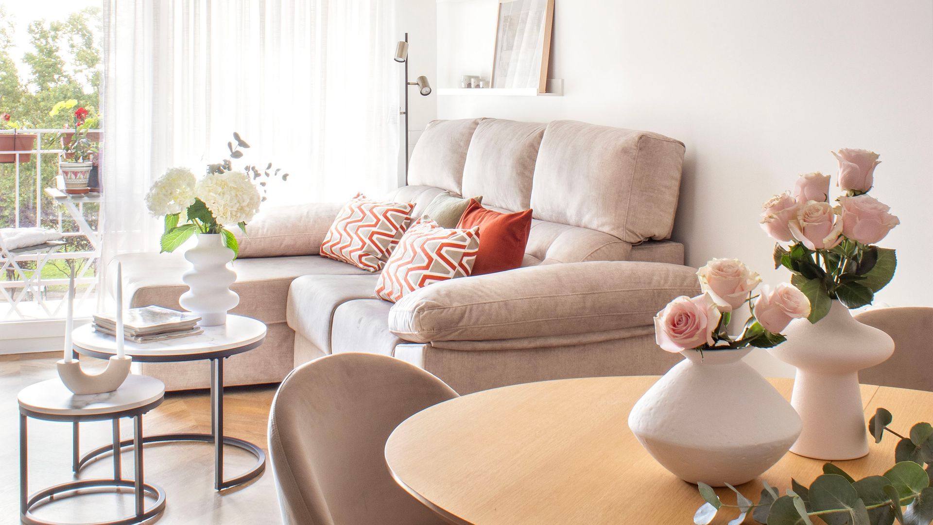 Salón comedor con salida a la terraza, cojines tierra, mesas auxiliares metálicas, sofá beige, cortinas blancas tipo visillo