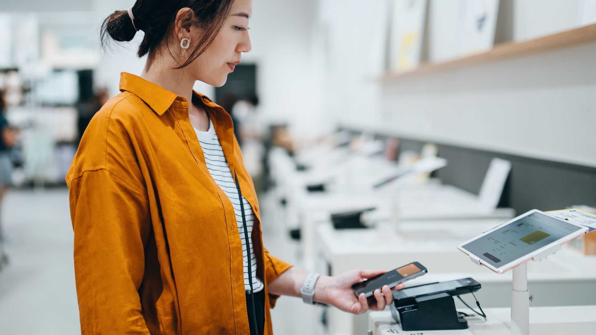 Mujer asiática pagando en un terminal de tecnología en una tienda.