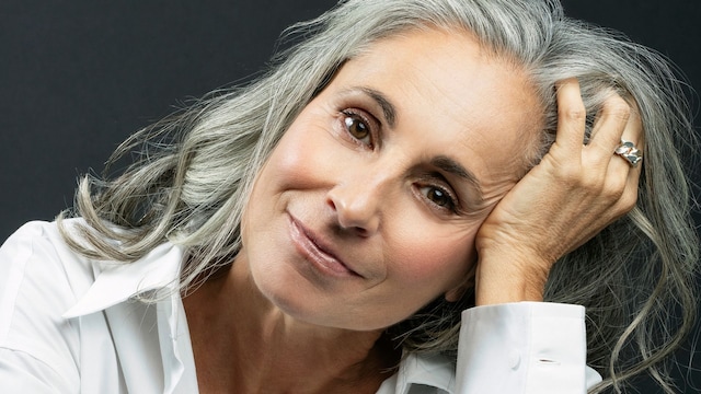 Mujer sonriente con la mano en el cabello contra un fondo negro