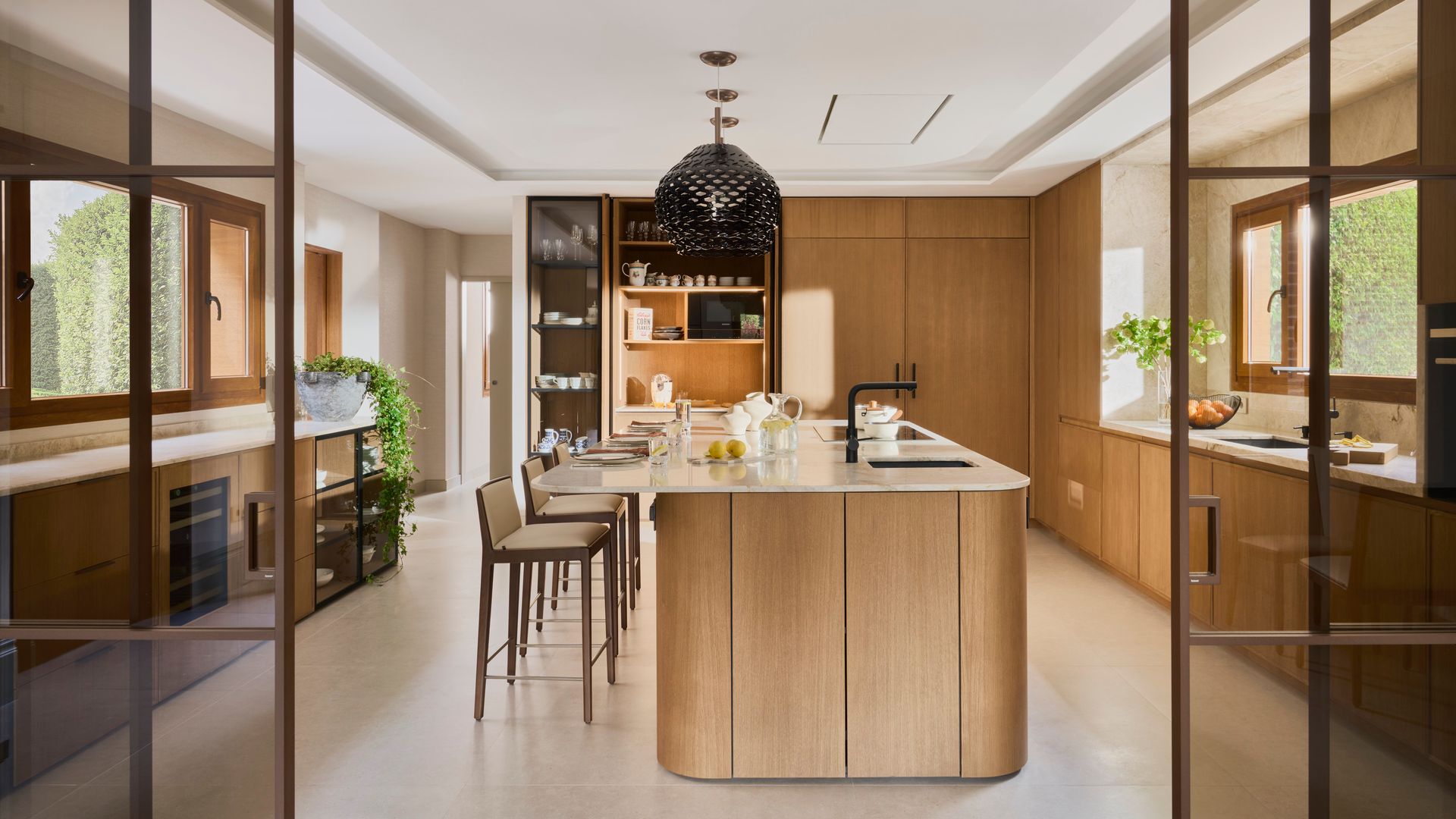 Cocina de madera lujo con isla central con taburetes, lámpara de techo negra, ventanales con el marco madera