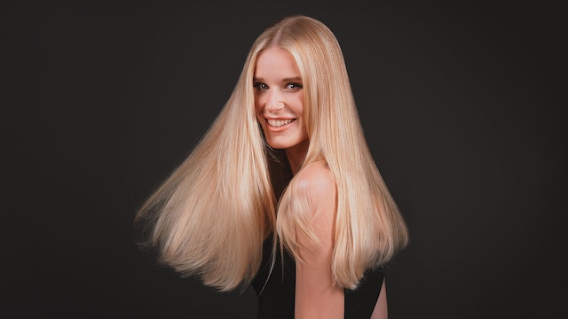 Mujer rubia con cabello largo brillante mirando a cámara sonriente