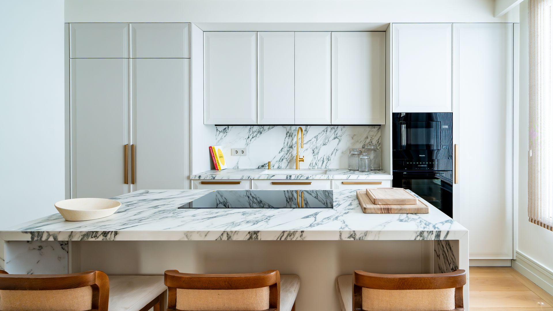 Cocina blanca con muebles hasta el techo, isla de mármol, taburetes de madera, antepecho de mármol