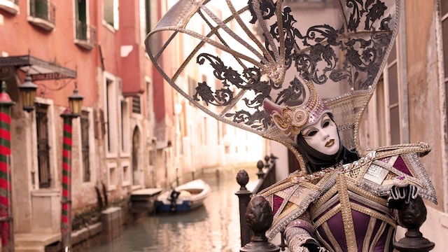 Mujer con disfraz medieval típico de los Carnavales de Venecia en un canal de la ciudad.