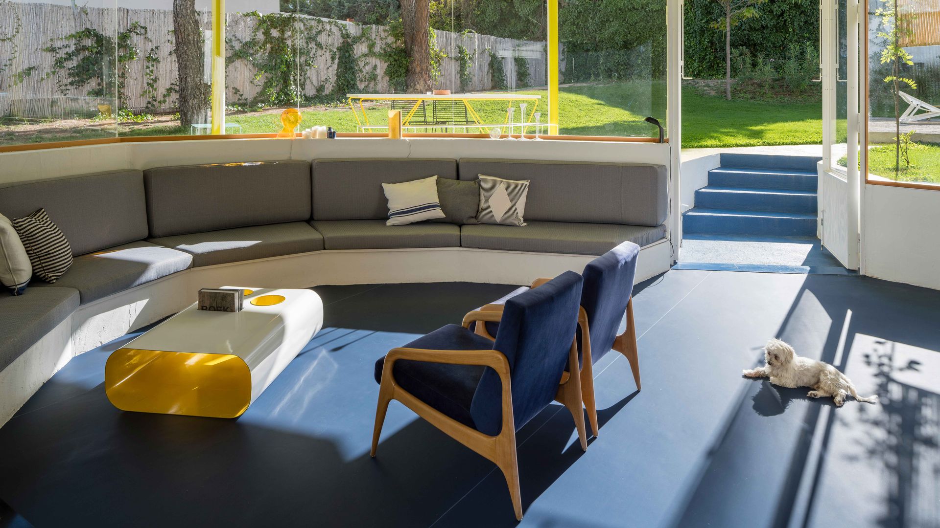 Salón con banco de obra, suelo azul, mesa de centro blanca y amarilla, butacas azules