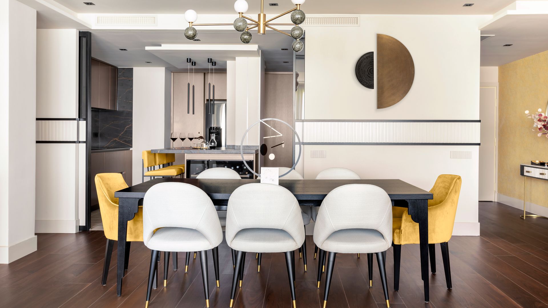 Comedor con suelo de madera oscura, mesa negra, sillas tapizadas en colores claros y amarillos, lámpara de techo 