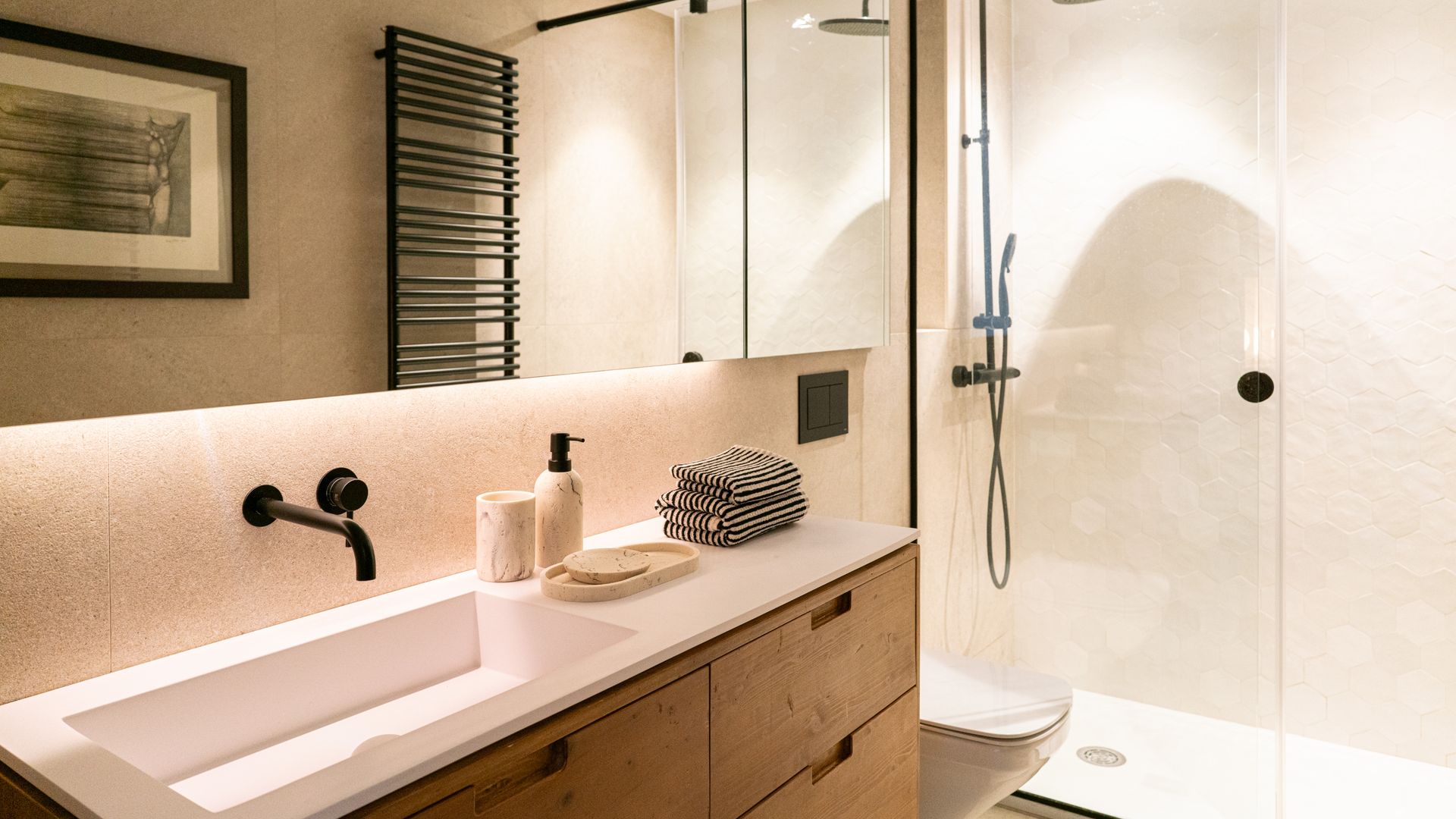 Baño con paredes de mármol, espejo, ducha, mueble de madera, grifería negra