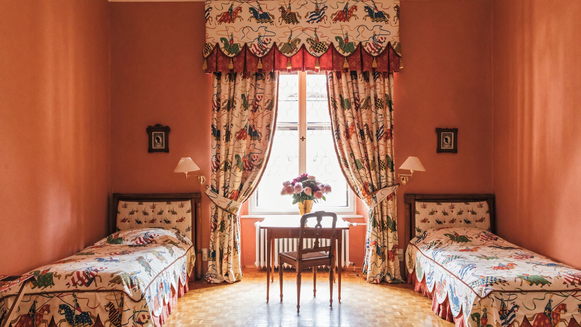 Dormitorio con dos camas, mesa, silla y ventana con cortinas decorativas.