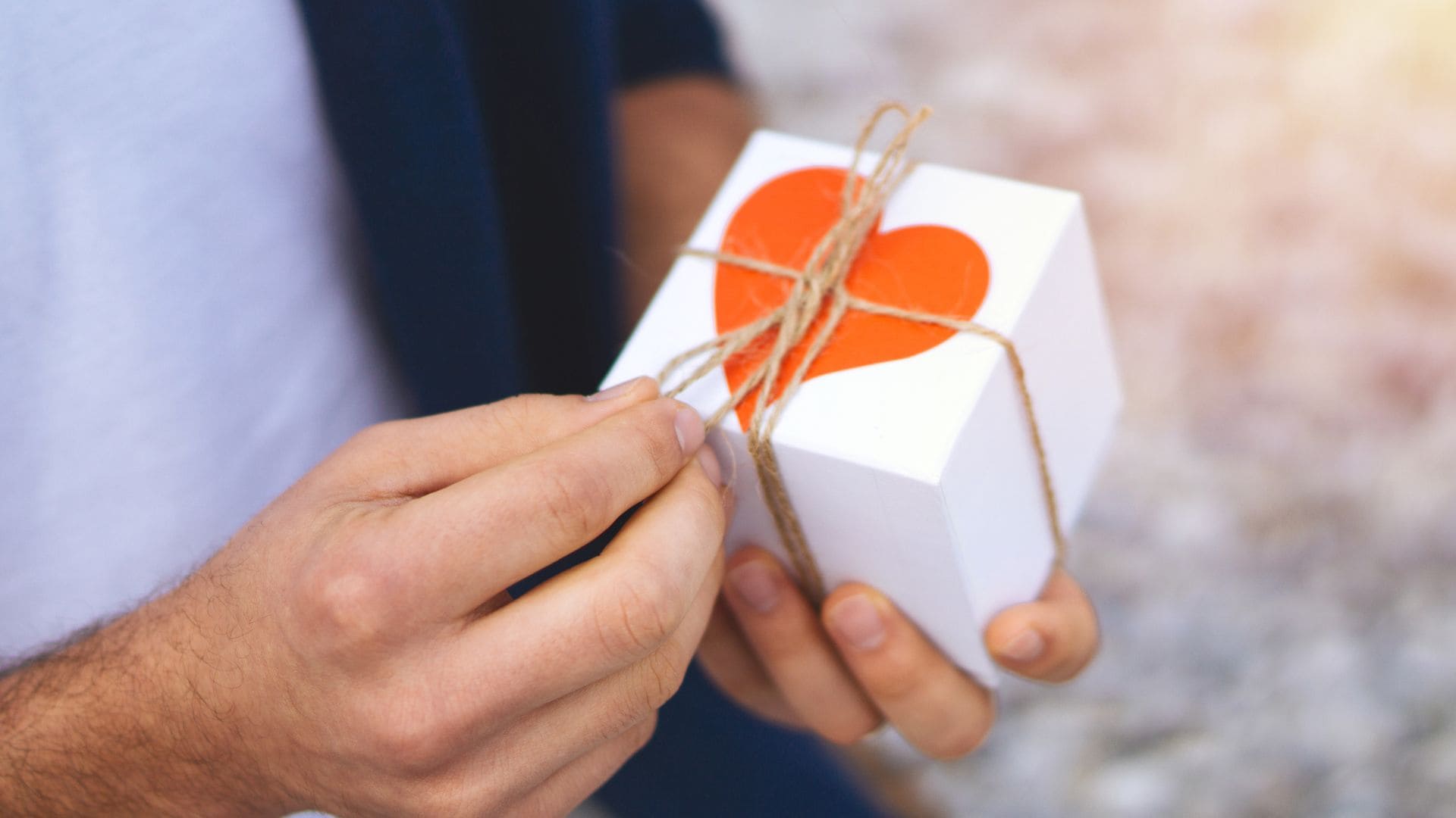 Hombre abriendo una caja o regalo con un corazón por San Valentín. Plano detalle de sus manos.