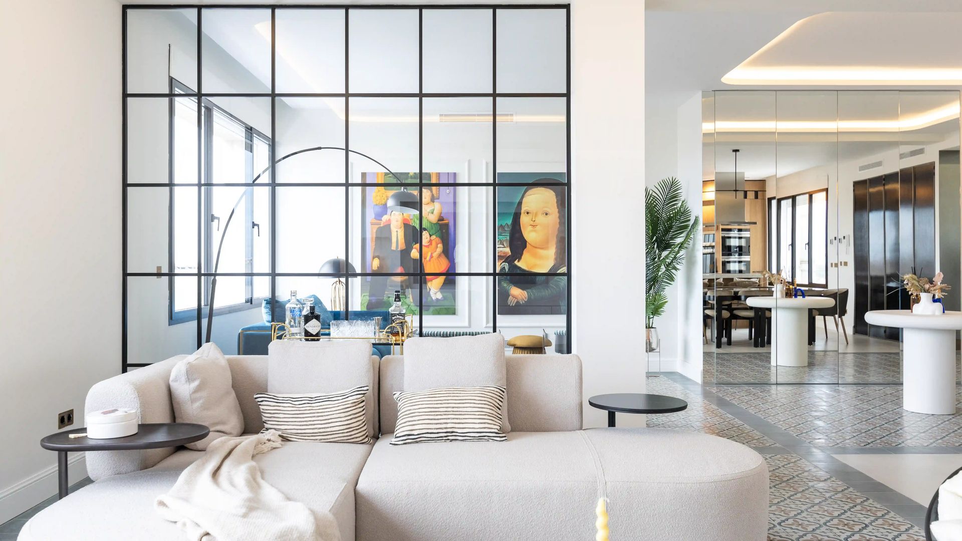 Salón con sofá blanco, tabique de cristal con cuarterones negros, suelo hidráulico