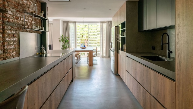 Cocina alargada abierta al comedor con pared de ladrillos, muebles de madera, encimera negra, campana de techo