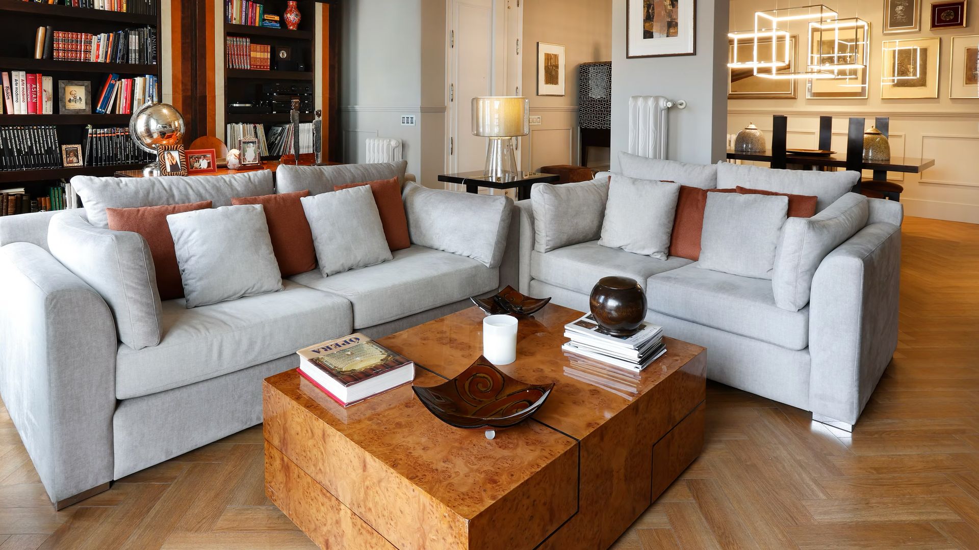 Salón comedor con suelo de madera, librerías de madera oscura, mesa de centro de madera, sofás grises