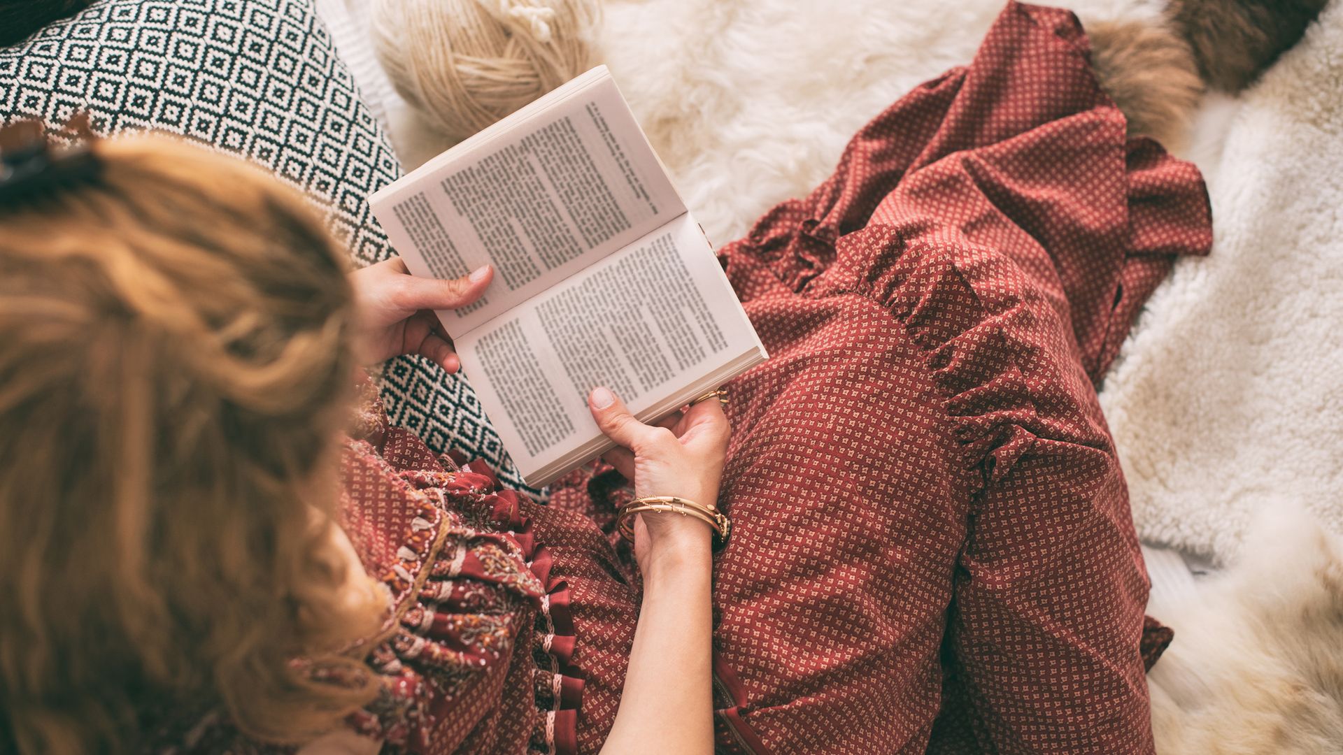Mujer joven leyendo un libro sobre una alfombra, con un vestido de puntos en rojo y volantes. La foto es desde arriba.