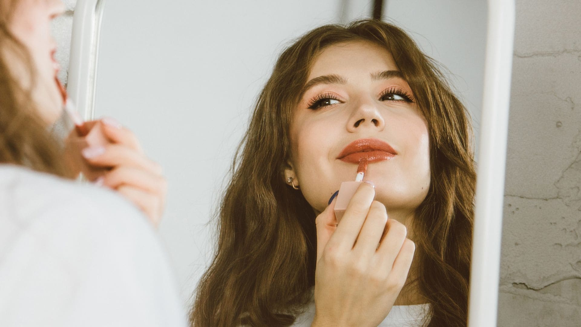 Mujer joven pintándose los labios frente a un espejo de pie