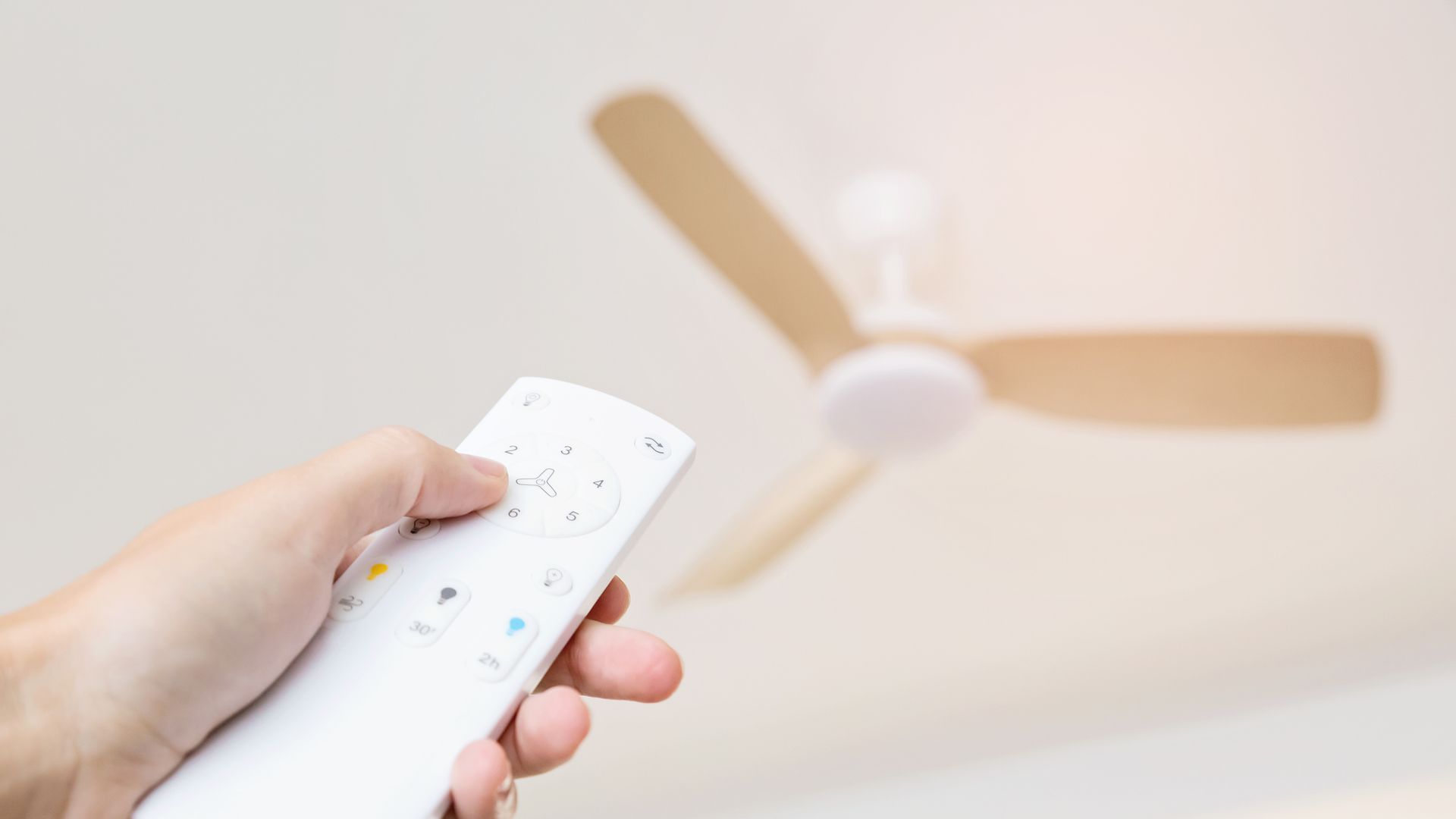 Mano con mando a distancia blanco activando un ventilador de techo